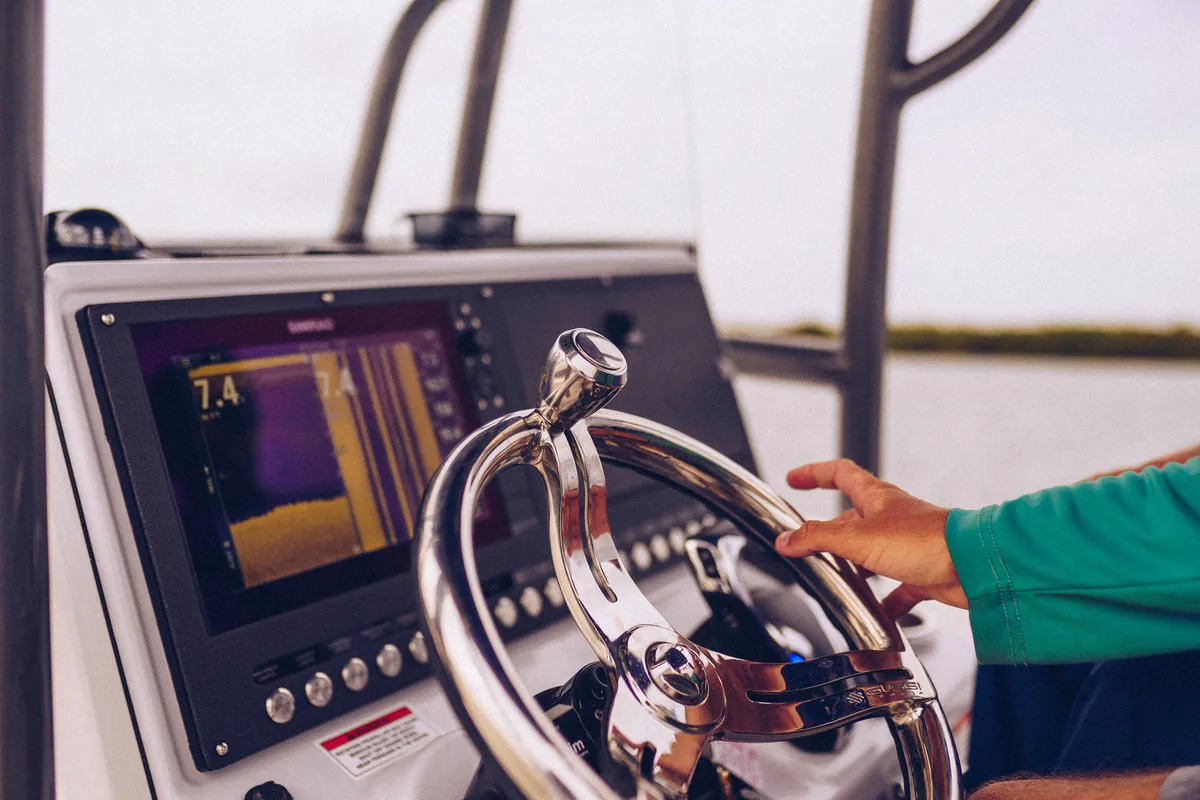 Captain's hand on the wheel beside a fish finder